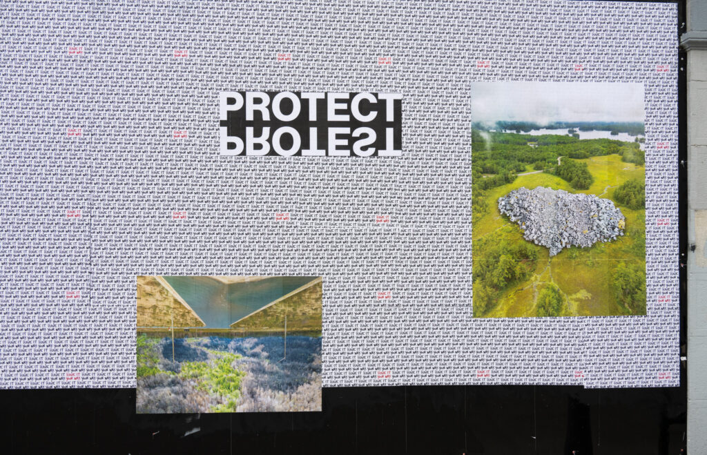 Colour Photograph of photo montage art and the words PROTECT PROTEST in white text on black pasted up on a black wall with white paper and the words "have it your way" repeated in the background.