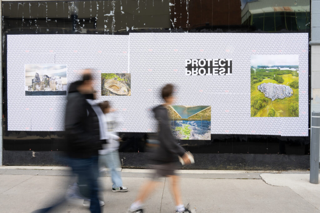 Colour photograph of people walking by a wall of pasted up art on the hoarding over storefronts.