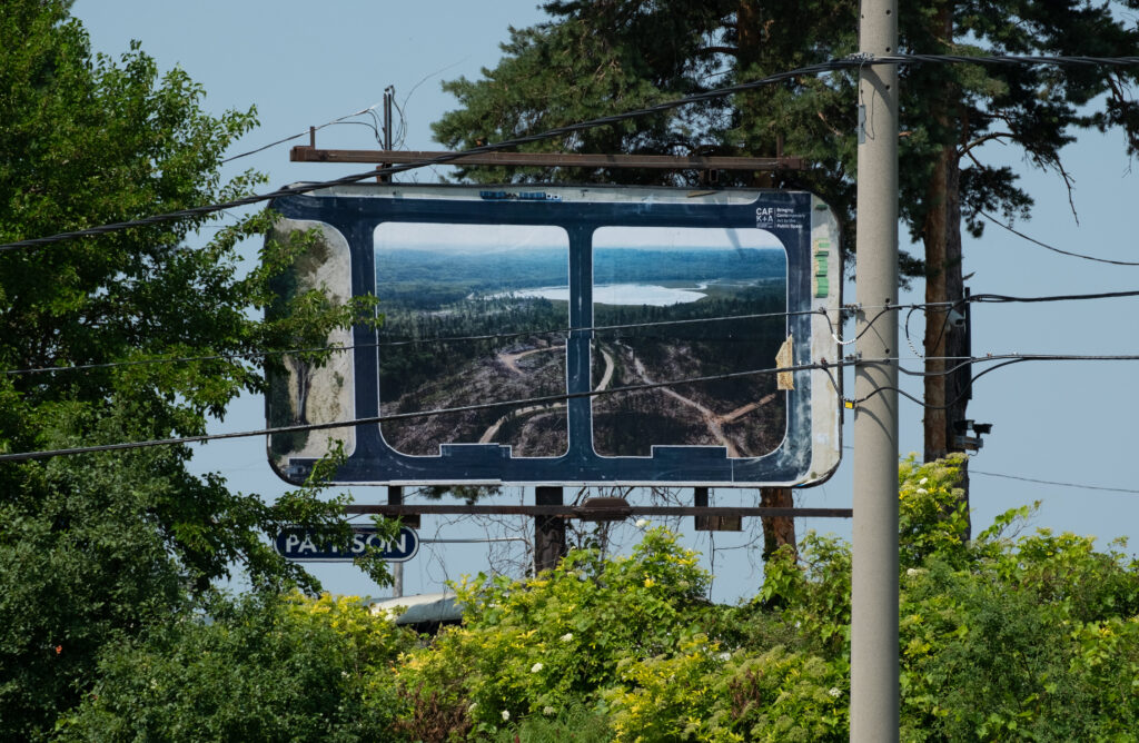 A colour photograph of a Pattison billboard of a photomontage of two photographs. The billboard is surrounded by trees.