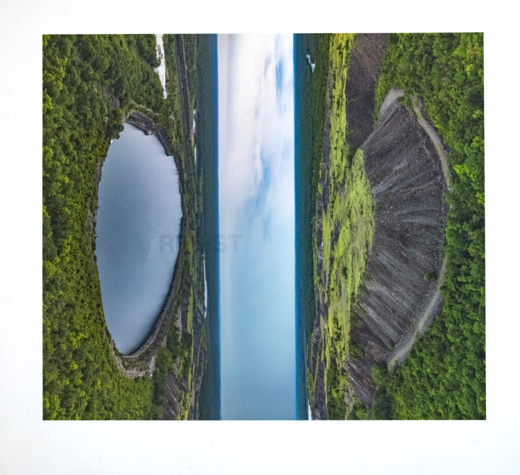 A colour photomontage of two landscape images rotated to join in the sky at the vertical center. on the left is an image of a oval shaped body of water surrounded by trees, on the right is a similar scale oval shaped mound of earth surrounded by trees.
The word RESIST is screenprinted in clear ink on the image.