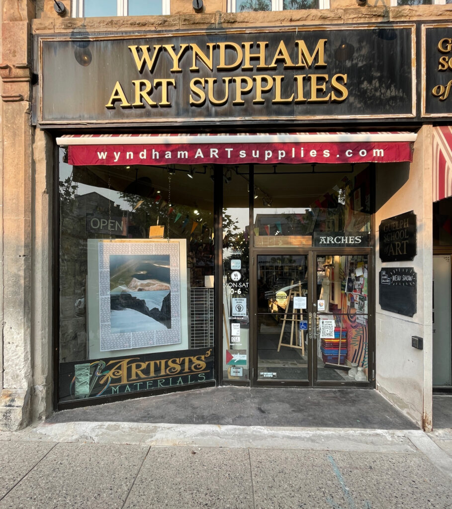 A colour photograph of a storefront "Wyndham Art Supplies" with art installed in the window.