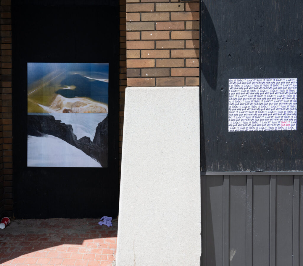 Colour Photograph of a boarded up storefront with text art and photomontage pasted up on a the blacked hoarding of what was a window. The words Have it Your Way are repeated over and over in black text on the right and on the left, a colour photomontage is pasted up on the boarded up doorway.