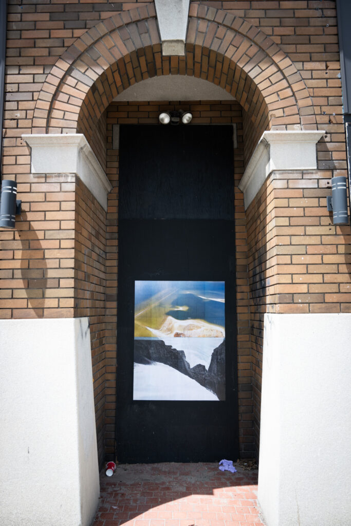 A colour photograph of a photomontage of ice and water pasted onto a boarded up doorway painted black.