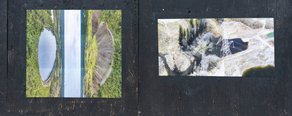 A colour photograph of 2 photomontages, one of a body of water and earth, and the other land and powerlines pasted onto a boarded up surface painted black.